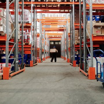 inside a factory with shelving around a person walking down a hallway